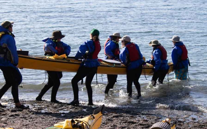 a group of students carry a kayak into the water on an outward bound expedition in the pacific northwest